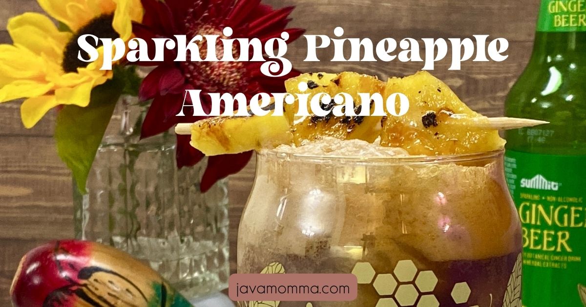A refreshing Sparkling Pineapple Americano served in a tall glass over crushed ice, topped with a slice of brûléed pineapple and bubbles sparkling at the surface.