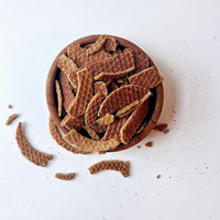 Thumbnail for A wooden bowl filled with Stroopwafel Crumbs – Irresistibly Crunchy Caramel Cookie Magic sits on a white surface, with extra caramel cookie bits scattered around.