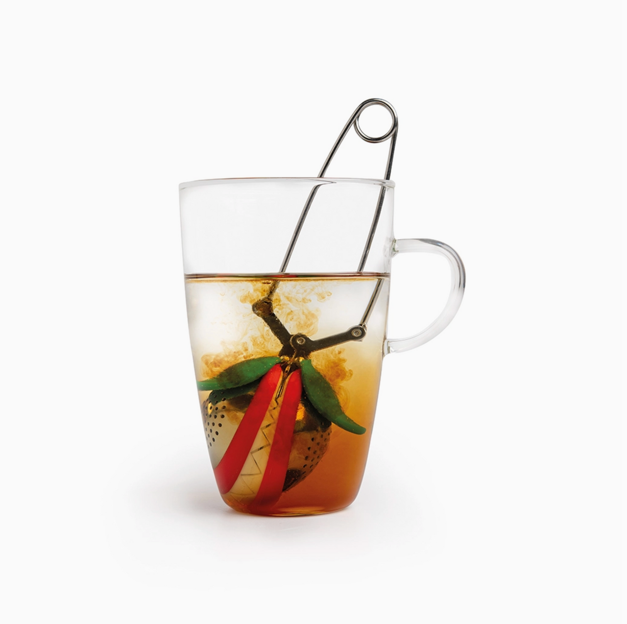 A glass mug with loose leaf tea brews as color swirls from the whimsical 🪴 Steep Fiend – The Loose Leaf Monster That Lives to Brew by OTOTO Studio, its strawberry-shaped infuser partially submerged and attached to a metal handle.