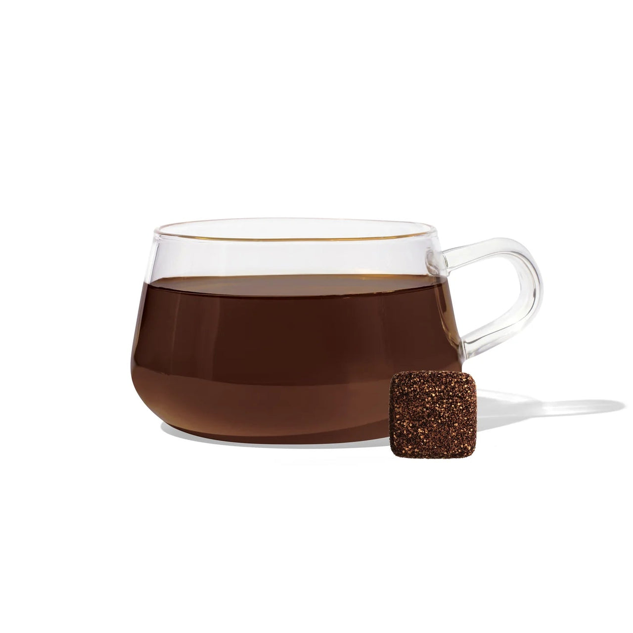 A clear glass cup filled with Pumpkin Spice Tea Drop – Cozy Up to Fall in a Cup 🎃☕🍂 sits on a white background, with a single brown tea cube placed beside it.