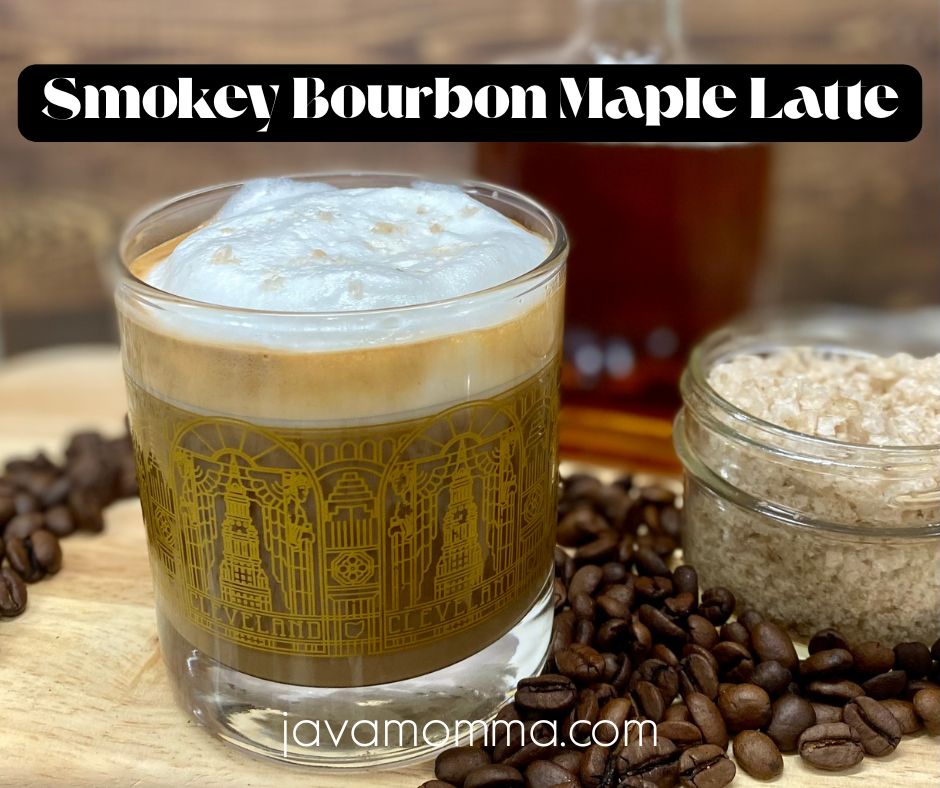 A cozy mug of Smokey Bourbon Maple Latte topped with frothed milk and a sprinkle of smoked salt, served on a wooden tray with a small jar of maple syrup and scattered coffee beans.