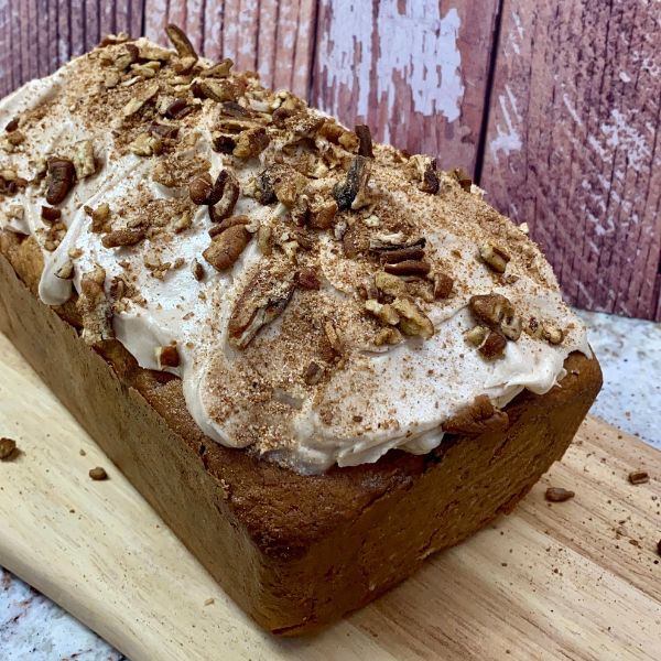 Whole frosted loaf cake with pecans and Pumpkin Spice Coffee in background.