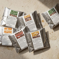 Thumbnail for Six Java Momma drink mix packets in silver foil spread across a light surface overhead, displaying a mix of mocha, cocoa, and frappe varieties.