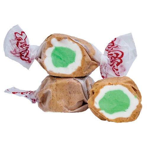 Three pieces of Apple Pie Salt Water Taffy - Freeze-Dried, Sweet & Spiced Candy Crunch are wrapped in white paper with red print, showing tan exteriors and a white and green layered center, one cut open to reveal the colorful inside.