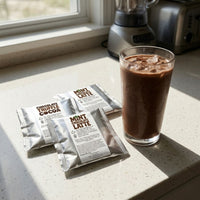 Thumbnail for A tall glass of blended mocha frappe on a kitchen counter beside Java Momma drink mix packets, with a blender visible in the background.