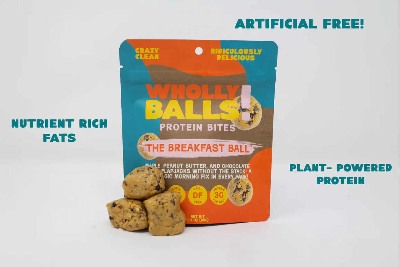 A pack of Maple Peanut Butter Chocolate Chip Wholly Balls stands upright, with three protein-packed bites in front. Text highlights ARTIFICIAL FREE!, NUTRIENT RICH FATS, and PLANT-POWERED PROTEIN—a perfect plant-based breakfast.