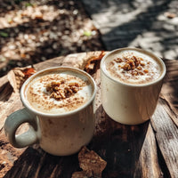 Thumbnail for Two mugs of creamy coffee topped with walnuts and cinnamon sit on a rustic wooden table, enhanced by a drizzle of Butter Pecan Skinny Syrup – Warm, Nutty, Southern-Inspired Indulgence 🧈🌰✨. Sunlight and autumn leaves add cozy vibes for relaxing moments.