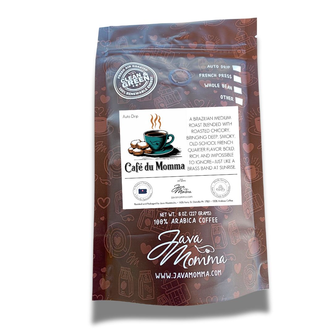 A brown, resealable coffee bag featuring the Café du Momma label. The label displays the clipart-style teal coffee cup with beignets, along with a description of the coffee: "A Brazilian medium roast blended with roasted chicory, bringing deep, smoky, old-school French Quarter flavor. Bold, rich, and impossible to ignore—just like a brass band at sunrise." The bag also features branding elements such as the "Java Momma" logo and website.