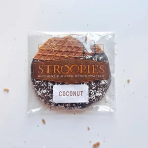 A Gluten Free Coconut Stroopie – Dark Chocolate Dipped with Toasted Coconut Bliss, featuring a coconut flavor label, is partially dipped in dark chocolate, sprinkled with toasted coconut flakes, and has a few crumbs nearby.