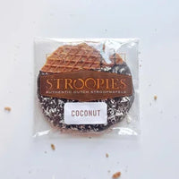 Thumbnail for A Gluten Free Coconut Stroopie – Dark Chocolate Dipped with Toasted Coconut Bliss, featuring a coconut flavor label, is partially dipped in dark chocolate, sprinkled with toasted coconut flakes, and has a few crumbs nearby.