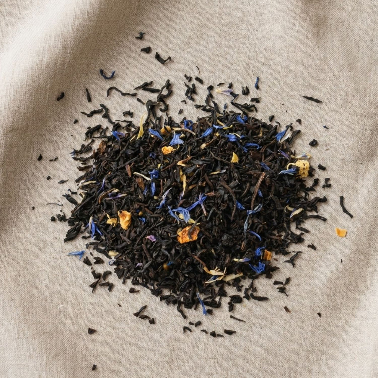 Loose leaf Earl Grey tea blend with black tea, blue cornflower petals, and citrus pieces on neutral linen background.