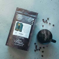 Thumbnail for Fade to Black Coffee package with a mug and scattered beans on a textured surface