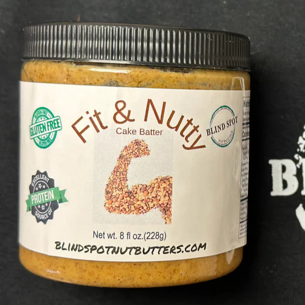 A jar of Fit & Nutty – 🎂 Vanilla Cake Batter Nut Butter – Sweet Gains & Birthday Vibes, featuring a nut-arm label. It’s paleo friendly, gluten free, high protein, and part of the Blind Spot high protein nut butter range.