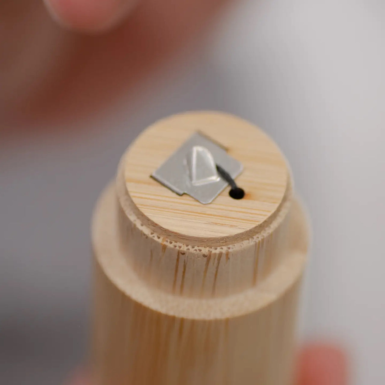 A hand holds the Bamboo Floss Holder with Charcoal Floss—an eco-friendly, gentle, and refillable oral care tool made from bamboo with a metal blade, ideal for sustainable dental hygiene.