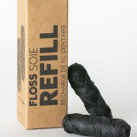 Thumbnail for A No Tox Life® Charcoal Floss Refills – 2-Pack box stands upright beside two black eco-friendly floss spools, all set on a white surface.