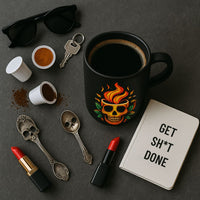 Thumbnail for A flat lay of a black coffee mug featuring fiery skull artwork, surrounded by single-serve coffee pods, spilled grounds, skull-shaped spoons, red lipstick, keys, sunglasses, and a notebook reading “GET SHT DONE,” all styled on a charcoal surface.*
