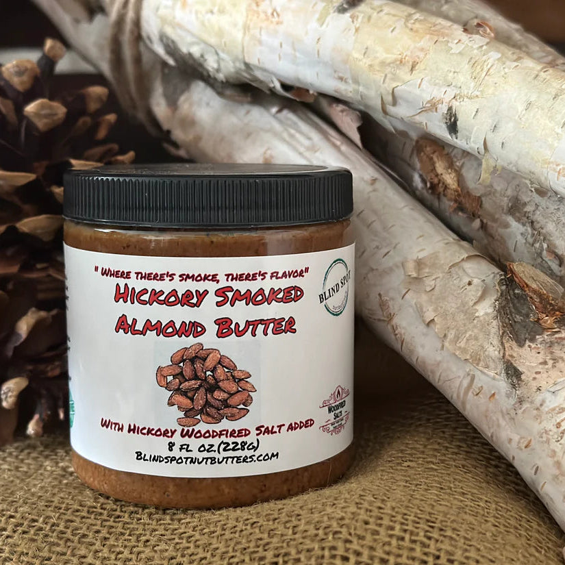 Jar of hickory smoked almond butter with a pine cone and log in the background