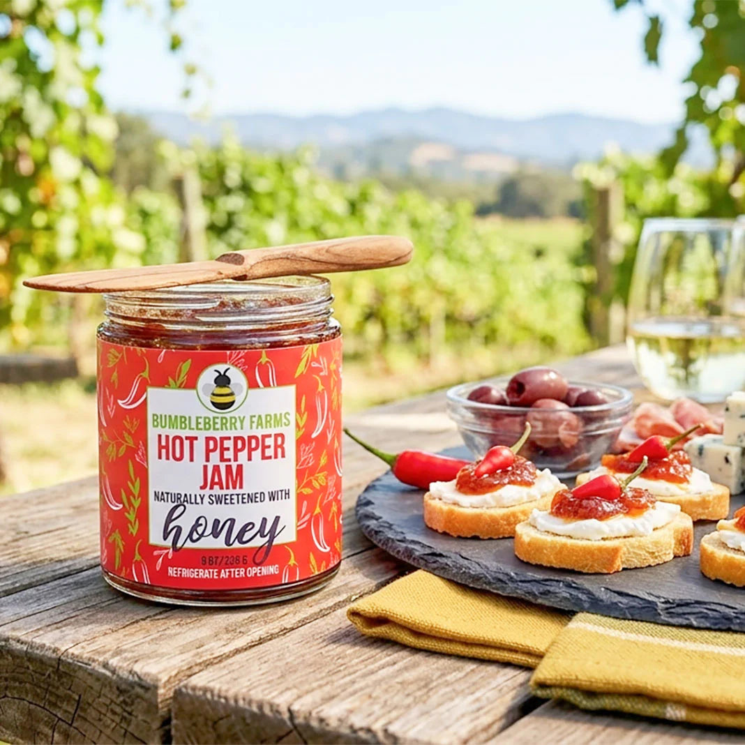 Jar of Bumbleberry Farms hot pepper jam on a table with appetizers and a scenic background