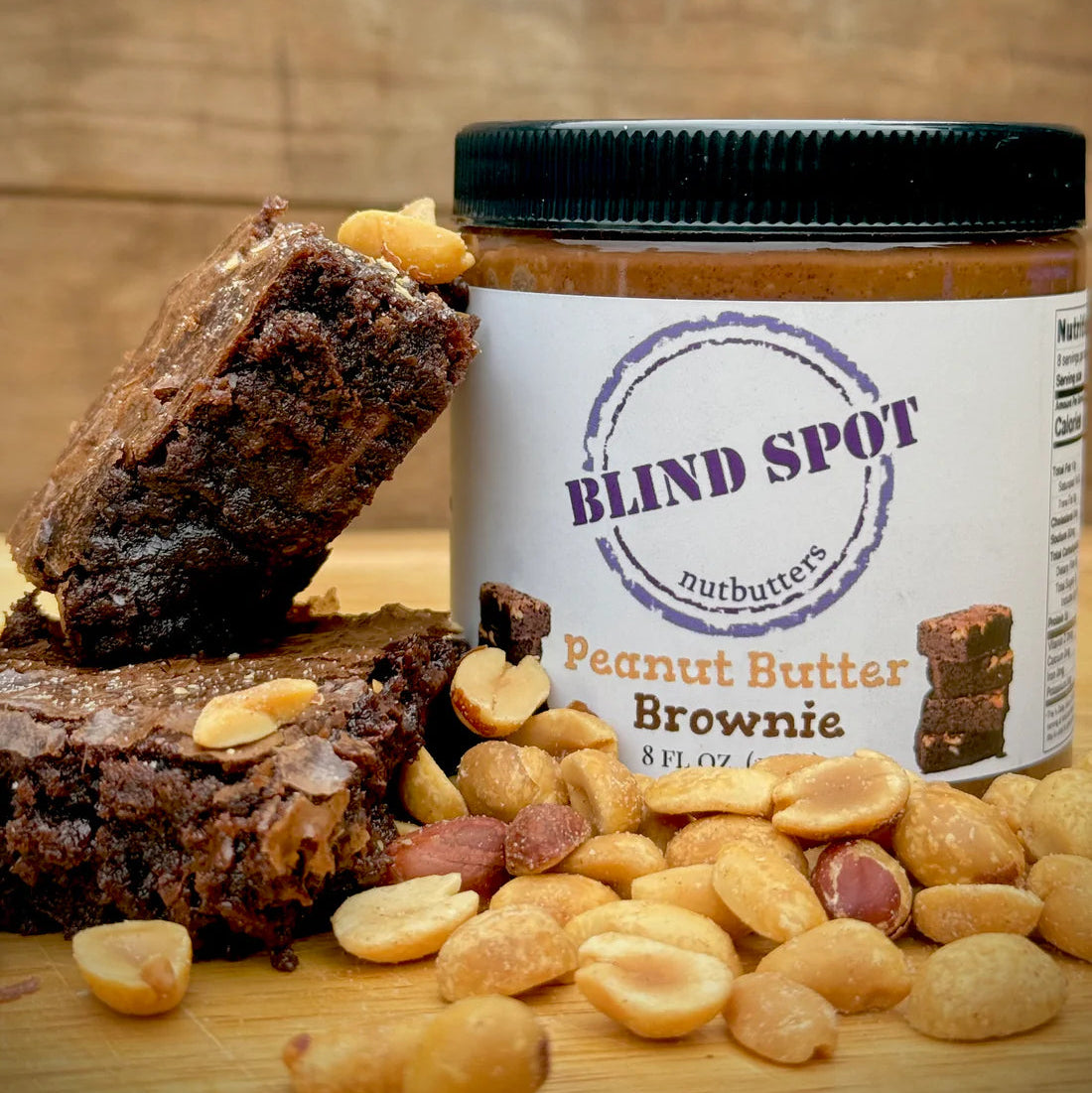 Jar of Blind Spot Peanut Butter Brownie with brownies and peanuts on a wooden surface