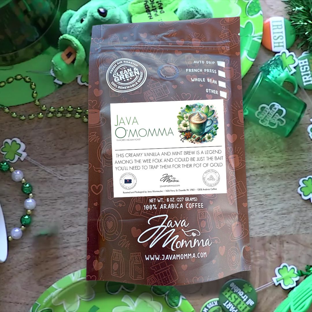 A branded bag of Java O’Momma coffee stands against a festive St. Patrick’s Day backdrop, featuring shamrocks and golden accents. The packaging highlights its creamy vanilla and mint flavors, perfect for a lucky brew.