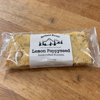 Thumbnail for A packaged slice of Northwest Biscotti Lemon Poppyseed Handcrafted Biscotti on a wooden tabletop. The biscotti is sealed in clear plastic packaging with a white paper label showing the brand name and product type.