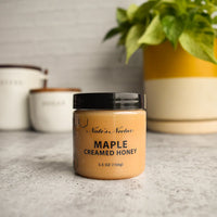 Thumbnail for A jar of Nate’s Nectar Maple 🍁 Creamed Honey – Cozy, Sweet & Spreadably Smooth sits on a gray countertop, with two labeled kitchen canisters and a green potted plant in the background.