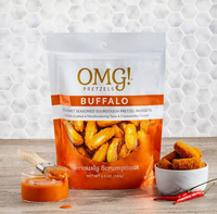Thumbnail for A bag of OMG Pretzels - Buffalo Sourdough Pretzel Nuggets is on a table next to a bowl filled with the spicy nuggets and a wooden spoon, with orange sauce spilled nearby, all on a white hexagon tile background.