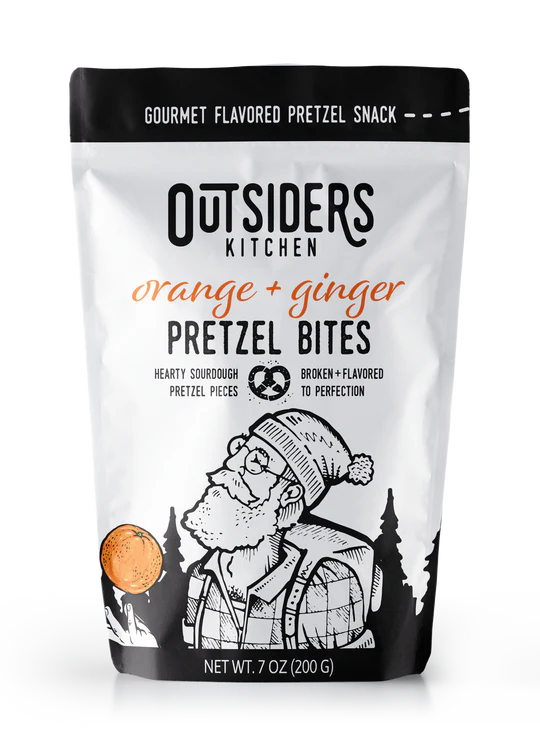 A white 7 oz (200 g) bag of Orange + Ginger Pretzel Bites – Zesty, Creamy, and Boldly Delicious 🍊🔥 features sourdough bites and an illustrated bearded man in glasses and a winter hat among trees and a pretzel.