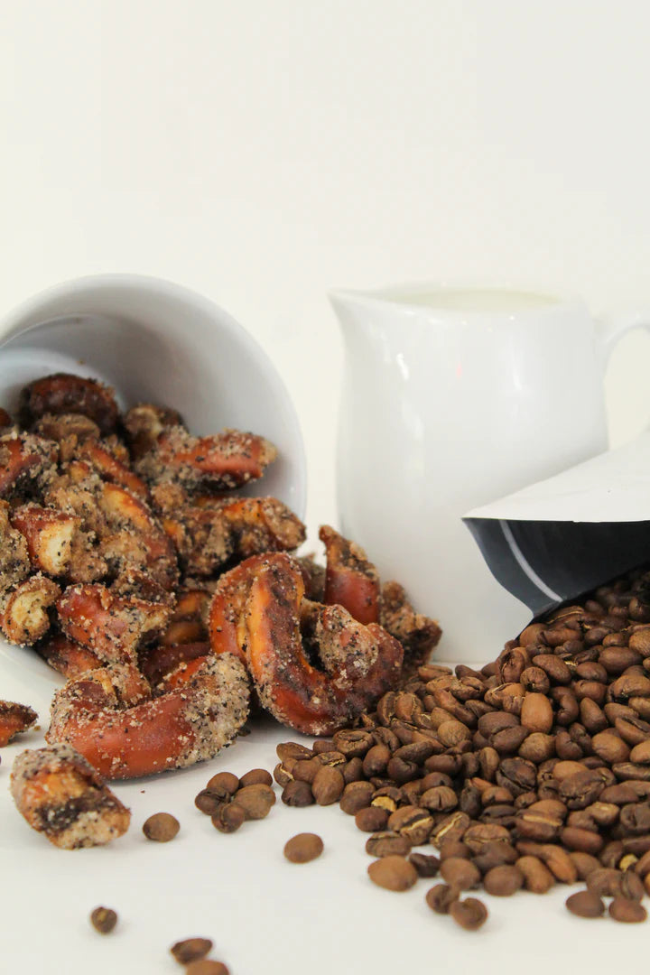 A white cup spills Coffee + Cream Pretzel Bites – Sweet, Salty, and Seriously Addictive ☕✨ next to scattered coffee beans, with a white pitcher and bowl in the background for this tempting small batch snack scene.