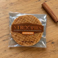 Thumbnail for A packaged round Stroopies gluten-free Dutch stroopwafel cookie on a wooden surface, with a cinnamon stick prop in the background.