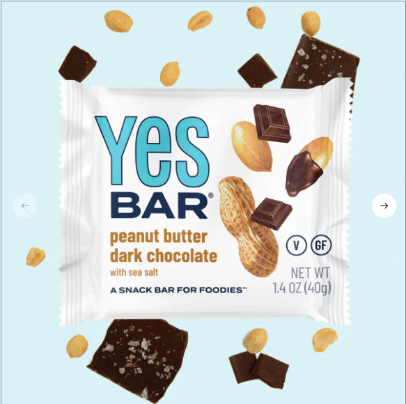 The Peanut Butter Dark Chocolate YES Bar® – A Classic Crave, Upgraded is shown in its wrapper with chocolate pieces, peanuts, and a peanut shell on a light blue background. The label highlights that it’s vegan and gluten-free.