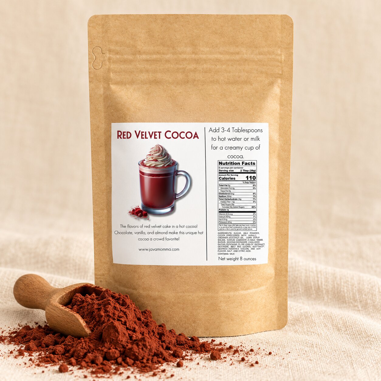 A kraft paper stand-up pouch labeled Red Velvet Cocoa stands on a beige fabric surface with a wooden scoop of cocoa powder in front. The package shows a mug of cocoa with whipped cream and includes nutrition facts and product description text.
