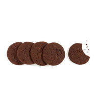 Thumbnail for Five Chocolate Cacao Nib Cookies from the Rich, Crunchy, & Full of Cocoa Love box🍫 by Rustic Bakery are lined up on a white background. The last cookie, made with premium cocoa, has a bite missing and crumbs nearby.