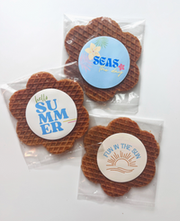 Thumbnail for Three Flower-Shaped Summer Gram Original Stroopie Singles – Classic Caramel are each wrapped in clear packaging with round, colorful summer-themed labels—Seas the Day, Hello Summer, and Fun in the Sun—on a white background.