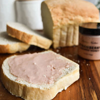 Thumbnail for A slice of white bread with light pink cream sits on a wooden surface beside more slices, a loaf, and a jar of Nate’s Nectar Strawberry Creamed Honey 🍓 – sweet, fruity, and ready to spread.