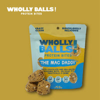 Thumbnail for A package of The Mac Daddy – White Chocolate Macadamia Wholly Balls | Plant-Based Protein Snack is shown with a few bites in front. The blue and yellow pack highlights its gluten-free, dairy-free, plant-based features and 3g protein per serving.