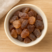 Thumbnail for Amber Sugar Crystals: Irregularly shaped amber pieces in a small white bowl on a light wooden surface beside a beige cloth—ideal as a natural tea sweetener.