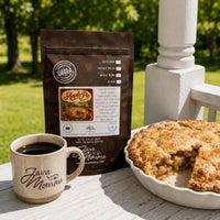 Thumbnail for Java Momma apple pie coffee package with a cup of coffee and apple pie on a wooden surface outdoors.