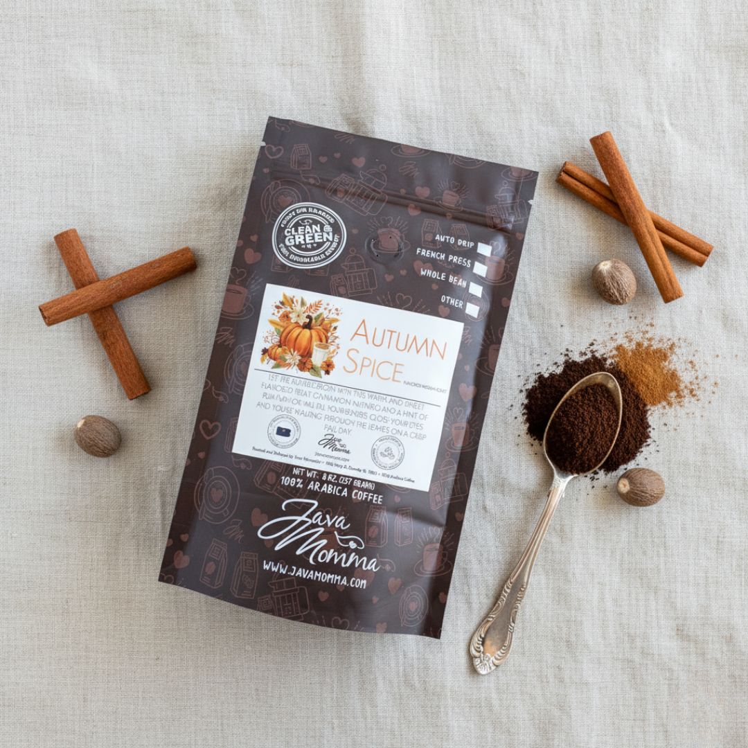 A bag of Autumn Spice Flavored Coffee, a rich seasonal blend, rests on a textured surface with cinnamon sticks, whole nutmeg, and a silver spoon holding ground coffee next to a small pile of grounds.
