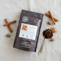 Thumbnail for A bag of Autumn Spice Flavored Coffee, a rich seasonal blend, rests on a textured surface with cinnamon sticks, whole nutmeg, and a silver spoon holding ground coffee next to a small pile of grounds.