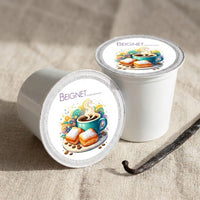 Thumbnail for Two white coffee pods with 'Beignet' branding featuring a coffee cup and beignets on a beige fabric background.