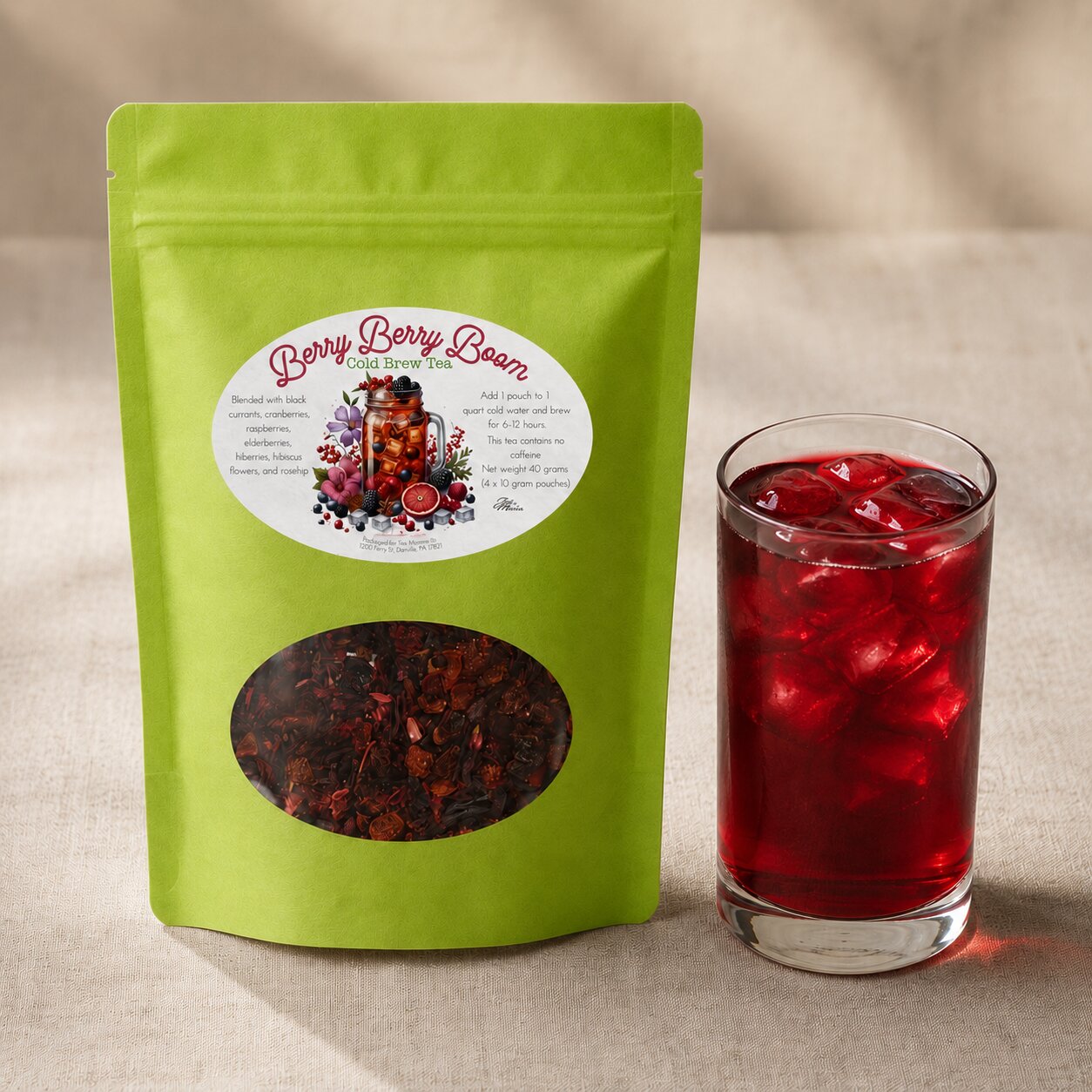Green tea package labeled 'Berry Berry Boom' next to a glass of iced berry tea on a beige background