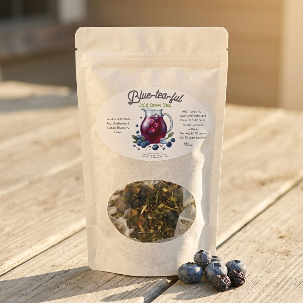 Tea package labeled 'Blue-tea-ful' with a clear window showing tea leaves, placed on a wooden surface with blueberries beside it.