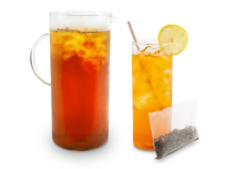 Iced tea with lemon slices in a glass and a pitcher, with a tea bag on a white background.