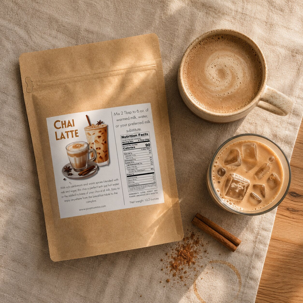 A kraft paper stand-up pouch labeled Chai Latte is arranged on a beige cloth with two cups of iced and hot coffee, plus cinnamon sticks and a few coffee rings on the surface.