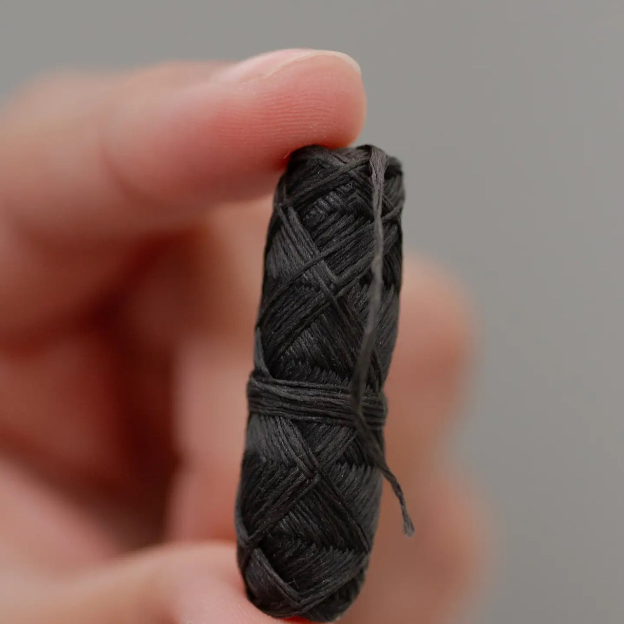 A hand holds the Bamboo Floss Holder with Charcoal Floss—an eco-friendly, gentle, and refillable oral care essential—against a plain light gray background.