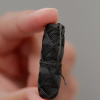 Thumbnail for A hand holds the Bamboo Floss Holder with Charcoal Floss—an eco-friendly, gentle, and refillable oral care essential—against a plain light gray background.
