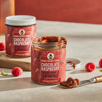 Thumbnail for An open jar of Chocolate Raspberry Honey Cream Spread 🍫 – Award-Winning, Rich & Fruity Chocolate Bliss sits with a knife covered in the creamy spread, while another jar and fresh raspberries are displayed in the background.