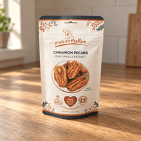 Thumbnail for A stand-up pouch of 'Nuts on the Run' Cinnamon Pecans Pure Vanilla Extract standing on a wooden tabletop in a warm, sunlit kitchen setting.