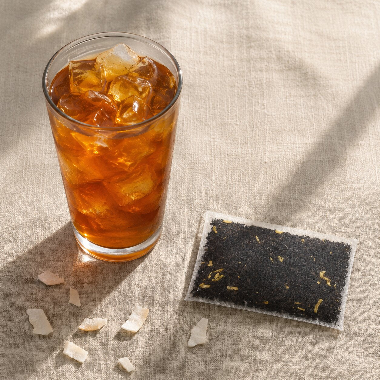 Glass of iced tea with a coco nuttea tea bag and tea leaves on a textured surface